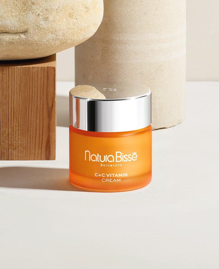 C+C Vitamin Cream. El empaque es color naranja con una tapa metálica. El producto está ubicado entre decoración diáfana